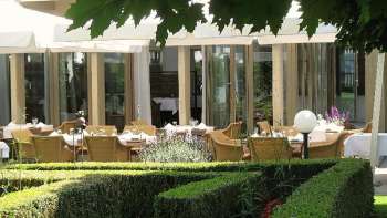 Terrazza soleggiata del giardino del ristorante Vivid con tavoli apparecchiati e vista sul verde