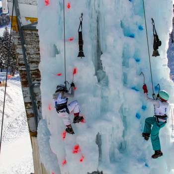 Due bambini che si arrampicano sul ghiaccio sulla torre di arrampicata ghiacciata di Malbun con piccozze e caschetti