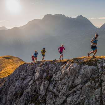 Gruppo di trail runner su una cresta rocciosa nelle montagne del Liechtenstein sotto il sole del mattino e l'impressionante scenario alpino