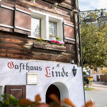 Facciata della Gasthaus Linde con struttura rustica in legno e persiane, decorata con fiori.