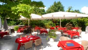 Vista esterna della terrazza con tovaglie rosse, circondata da alberi e ombrelloni.