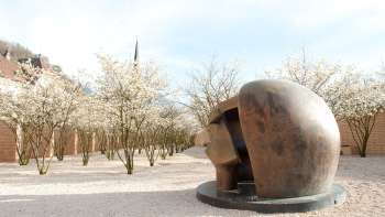 Scultura in bronzo "Figure in a Shelter" di Henry Moore nel Parco delle sculture di Vaduz - circondata da alberi in fiore in primavera.