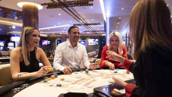 Atmosfera amichevole al tavolo da gioco: tre ospiti chiacchierano con il croupière nel Casinò Schaanwald, arredato con stile.