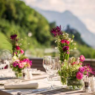 Tavola elegantemente apparecchiata con composizioni floreali su una terrazza con vista sulle Alpi - lo scenario perfetto per festeggiamenti o cene romantiche in Liechtenstein