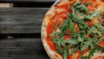 Pizza fresca con salsa di pomodoro e rucola, servita su un tavolo di legno rustico