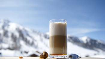 Bicchiere di latte macchiato su un piatto di legno sullo sfondo delle montagne innevate