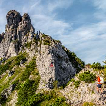 Escursionisti su un sentiero roccioso di montagna davanti a una cresta impervia con un cartello rosso e bianco