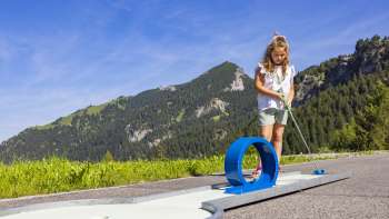 Ragazza concentrata su un percorso ad anello blu in un ambiente alpino mentre gioca a mini golf
