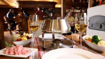 Primo piano di un set per fonduta di formaggio con pane fresco, verdure e vino in un contesto elegante