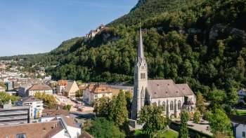 Vista aerea della Cattedrale di San Florin a Vaduz con il Castello di Vaduz sullo sfondo in una giornata di sole.