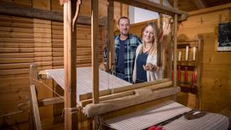 Una coppia osserva un telaio storico funzionante nel Museo Walser di Triesenberg, in Liechtenstein, circondato da pannelli in legno.