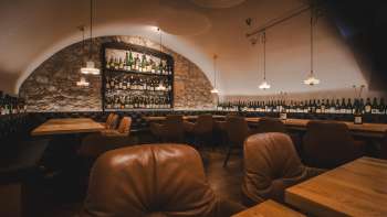 Interno suggestivo dell'WY Weinbar con scaffali illuminati, pareti in pietra naturale ed eleganti arredi nella cantina a volta.