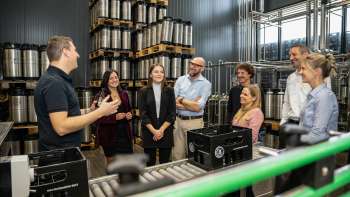 Gruppo di visitatori in visita guidata al magazzino delle botti del birrificio con spiegazioni da parte di un dipendente del birrificio.