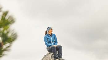 Rosaria Michaela Ackermann si siede su una roccia tra le montagne del Liechtenstein e guarda in lontananza