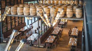 Invitante sala della birreria con lunghi tavoli in legno, decorazioni di botti e un'illuminazione elegante