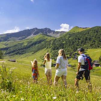 Una famiglia passeggia in un prato estivo in fiore a Malbun, nel Liechtenstein, e si gode la vista delle Alpi circostanti.