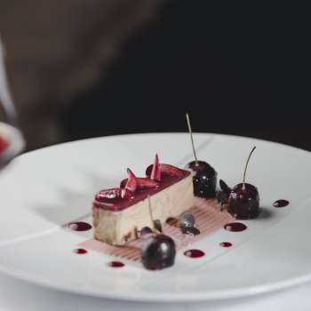 Elegante dessert su un piatto bianco, decorato con ciliegie e cioccolato