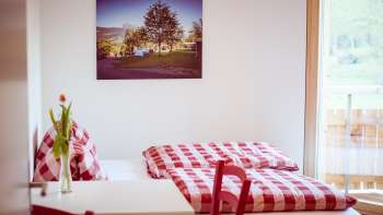 Accogliente camera doppia nella guest house del Camping Mittagsspitze con lenzuola e decorazioni a scacchi rossi e bianchi.