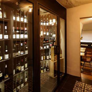 Moderna vetrina per vini con bottiglie pregiate nell'elegante WY Weinbar, vista sulla sala di degustazione adiacente.