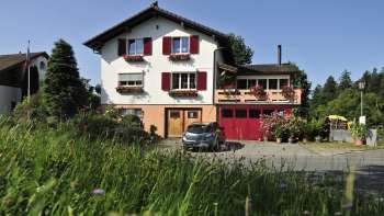 Incantevole vista esterna del Bed & Breakfast Büchel con persiane rosse e prato fiorito in primo piano.