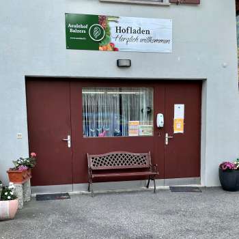 Ingresso del negozio della fattoria Aeulehof con cancello rosso, panchina e decorazioni floreali a Triesen, Liechtenstein.