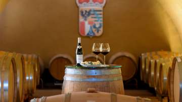 Vista della cantina con botti di legno e tavolo coperto con vino e formaggio presso le Cantine di Corte del Principe del Liechtenstein