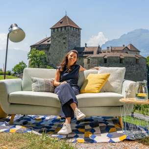 Donna seduta su un divano con vista sul castello di Vaduz e le montagne del Liechtenstein, ambiente moderno all'aperto con decorazioni