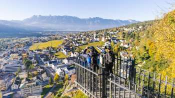 Escursionisti alla ringhiera del punto panoramico di Känzile con vista su Vaduz e sulle montagne circostanti.