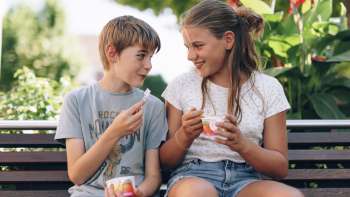 Vista di due bambini che gustano un gelato su una panchina di legno davanti alla gelateria Dolce Vita. Vista di due bambini che gustano un gelato su una panchina di legno davanti alla gelateria Dolce Vita.