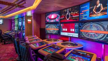Moderni tavoli da gioco con schermi digitali e diverse opzioni di roulette e giochi di carte nel Casinò Schaanwald, illuminato da un'atmosfera suggestiva.