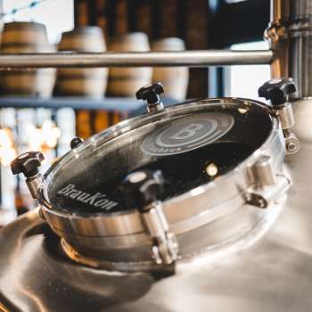 Primo piano di una finestra di visualizzazione rotonda su un bollitore lucido con una vista della sala di produzione della birra sullo sfondo.