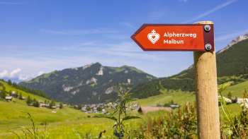 Cartello sentiero del cuore alpino con il villaggio di montagna di Malbun sullo sfondo