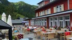 Terrazza soleggiata del ristorante con tavoli coperti, ombrelloni e vista sulle Alpi.
