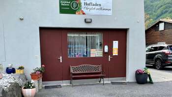Ingresso del negozio della fattoria Aeulehof con cancello rosso, panchina e decorazioni floreali a Triesen, Liechtenstein.