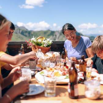 Famiglia che pranza insieme su una terrazza soleggiata a Sarreis, circondata da montagne e specialità regionali