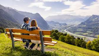 Coppia seduta su una panchina a Triesenberg e affacciata sulla valle del Reno in Liechtenstein con un impressionante panorama alpino