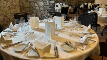 Tavolo rotondo elegantemente apparecchiato con tovaglie bianche, tovaglioli e menu davanti a un muro di pietra.