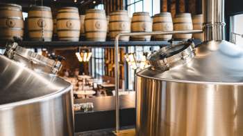 Vista di un moderno birrificio con serbatoi in acciaio inox scintillanti e botti di legno impilate sullo sfondo.