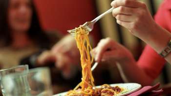 Una persona solleva gli spaghetti da un piatto con la forchetta nella Brasserie Burg - divertimento italiano in un'atmosfera conviviale.