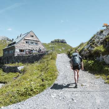 Escursionista con zaino che cammina lungo un sentiero di montagna verso il rifugio Pfälzerhütte nelle Alpi del Liechtenstein.