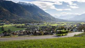 Autobus LIEmobil verde che percorre una strada tortuosa sopra il Liechtenstein con vista sulla valle del Reno e sulle Alpi circostanti
