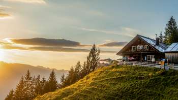Rifugio Gadafura su un prato di montagna soleggiato con vista sulle montagne e sul tramonto