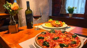 Primo piano di una pizza con pomodori, formaggio e basilico su un tavolo di legno, con un bicchiere di vino rosso sullo sfondo.