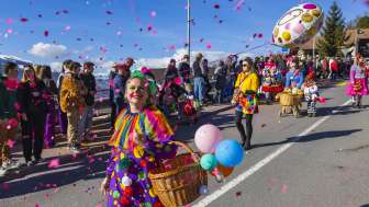 Clown vestito con coriandoli e palloncini alla sfilata di carnevale, spettatori a bordo strada.