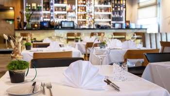  Tavola apparecchiata con gusto nel ristorante Alpspitz con vista sul bar sullo sfondo.