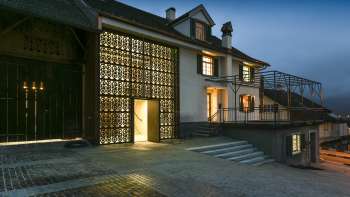 Moderna Kulturhaus Rössle illuminata a Mauren al tramonto, con facciata in vetro, ampliamento dell'edificio storico e piazzale pavimentato.