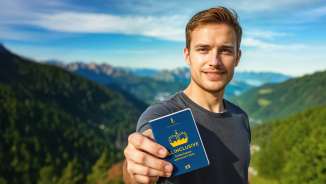Uomo mostra il «Pass attrazioni TUTTO INCLUSO» con panorama montano sullo sfondo