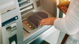 Donna che digita il codice PIN tenendo in mano il portafoglio davanti a un bancomat generico