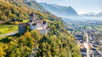 Vista del castello di Vaduz con la foresta dai colori autunnali e la città di Vaduz nella valle.