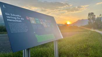 Pannello informativo sul campo alimentare di Vaduz con vista sulle Alpi al tramonto - un centro di apprendimento per l'alimentazione sostenibile nel Liechtenstein.